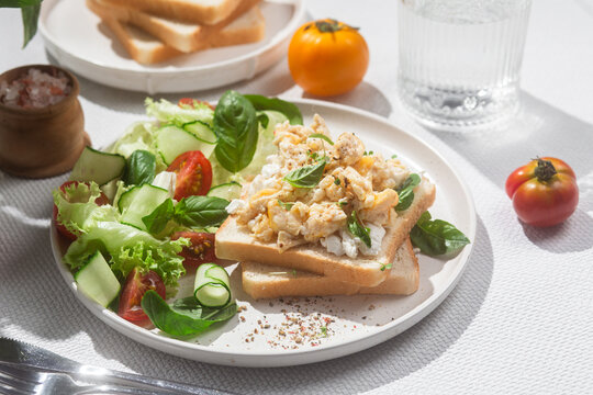 Scrambled eggs on toast bread with cucumber, tomato and herbs.White background.Healthy breakfast