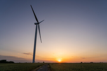 Obraz premium Wind turbine silhouette in rural field during colorful sunset – renewable energy and clean power concept with scenic countryside and environmental sustainability theme.