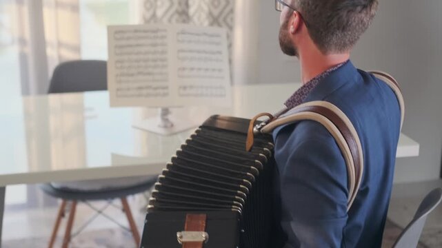 Back view of a man playing Bayan accordion in front of sheet music, recording a structured lesson for an online platform. Digital education, music tutorials, and content creation.