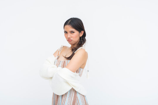 Pouting young Asian woman stares directly at camera with annoyed expression. Arms crossed, clearly sulking, frustrated, and irritated while keeping composed posture.