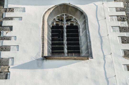 Detail gotisches Kirchenfenster mit Taubenabwehr und Schatten eines Blitzableiters an wei&szlig;er Wand der evangelischen Martinskirche in Neckartenzlingen