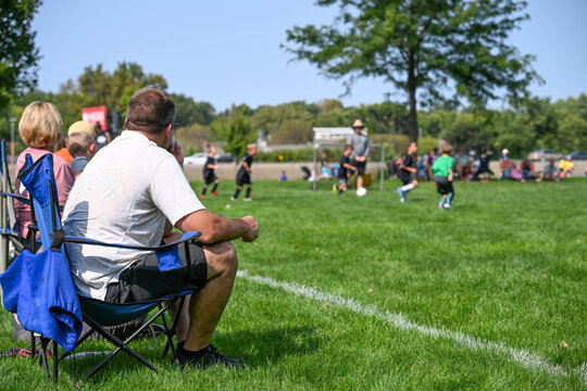 Parents enjoy a sunny day at a youth soccer match while supporting their kids on the field - Powered by Adobe