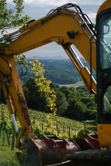 Big yellow excavator near the grape plantation in the village. Working in the countryside in the summer
