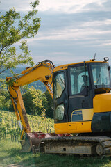 Big yellow excavator near the grape plantation in the village. Working in the countryside in the summer