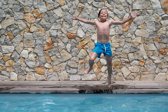 Caucasian eight year old boy having fun jumping with scary face into the water of a swimming pool enjoying summer vacation. Horizontal photo with copy space