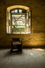 Sunlit abandoned room with broken window and old wooden chair, showcasing rustic decay and urban...