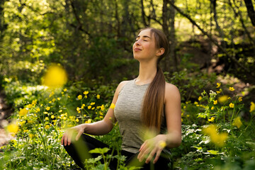 Portrait of young woman with closed eyes practicing meditation in lush green forest at sunlight, female in sportswear sitting in lotus pose in nature, wellness, mindfulness, zen energy outdoors