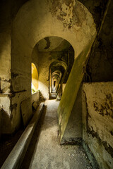Long abandoned corridor with arched ceilings and decayed walls illuminated by natural light in an...