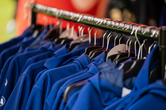 Row of blue sports hoodies hanging on clothing rack at outdoor market, casual athletic apparel display for sale during event, showcasing activewear merchandise for spectators