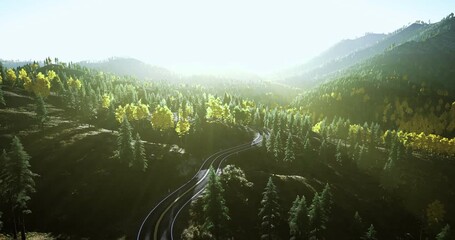 Winding train tracks curve through a vibrant landscape filled with lush green trees as the sun rises, casting a warm glow over the mountainous terrain and creating a serene atmosphere. - Powered by Adobe