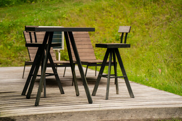 Modern outdoor patio furniture set on wooden deck in nature, minimalist table and bar stools with...