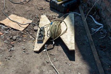Power strip and coiled extension cord rest on a makeshift wooden stand at a construction site,...