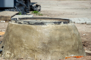 A concrete manhole cover base rests on the ground at a construction site, showing signs of wear under bright daylight