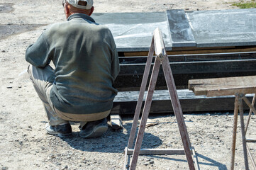 A skilled worker in casual attire crouches down, concentrating on wood planks at a construction site during the day