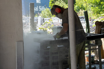 A worker skillfully shapes stone in an outdoor workshop, surrounded by greenery, while dust and sunlight create a vibrant atmosphere