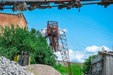 An old industrial tower rises amid lush greenery at a construction site, with heavy machinery and gravel piles scattered around under a bright sky