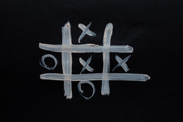 Drawn with light colors board game tic-tac-toe on black paper, play