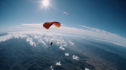 Spectacular aerial view of a skydiver descending with a bright red parachute over a vast mountain range under a clear blue sky with the sun shining brightly