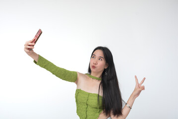Young Asian woman in a green top pouts her lips and makes a peace sign with her fingers in a...