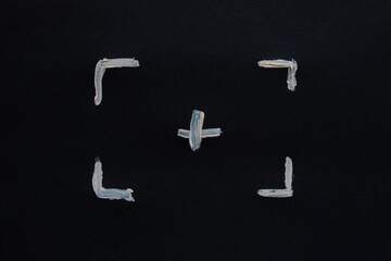 White painted frame and plus sign in the center from corners on black paper as a marking for...