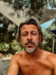 Ttanned man with stubble beard and blond hair enjoying summer garden with olive trees.