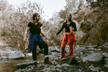 Two female hikers laughing and crossing a river in the forest