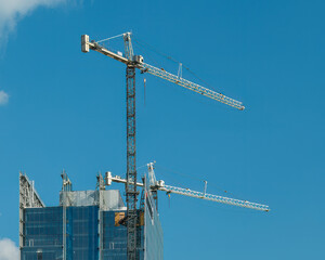 Cranes on a skyscraper under construction with a blue sky