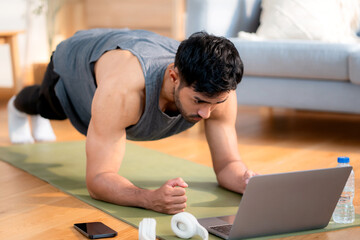 Young asian man doing plank exercise in living room at home while watching online workout tutorial...