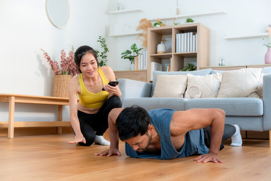 Young asian couple workout during woman hold smartphone encouragement to partner while man doing pushup with motivation, woman cheering man with exercise with strong and strength, self-care.