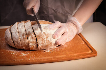 Baker Slicing a Freshly Baked Loaf of Bread on a Wooden Cutting Board