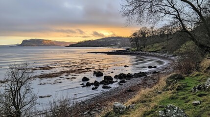 Serene coastal sunset scene, showcasing a tranquil bay with rocky shore, calm waters, and distant hills bathed in golden light