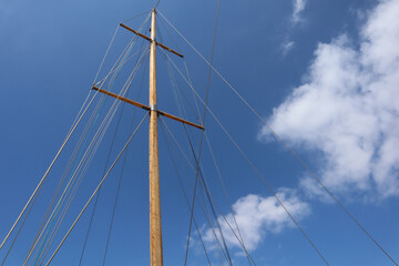 Wooden mast of a sailboat against the blue sky with clouds