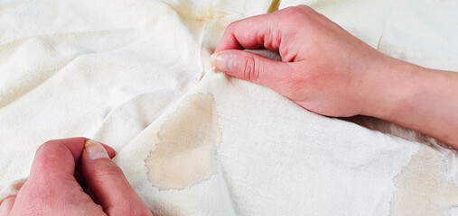 A woman is holding a white cloth with a stain on it. Dirty, stained cloth, thing, washing, dry cleaning.