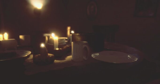 A cozy dinner table is arranged with plates and a cup amidst flickering candlelight. The warm atmosphere suggests an intimate meal in a subtly illuminated room.