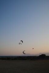 Several kitesurfers ride along the Turkish coastline at sunset. The silhouettes of kites contrast beautifully against the pastel evening sky. Ideal for themes of sport, freedom, beach holidays, and ac
