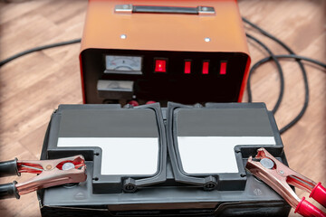 Charging car battery with home electricity charger.Jumper Cables with clamps attached to terminals.Automotive recovery,resuscitate low battery maintenance