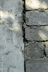 The junction of a gray concrete wall and gray block masonry. The vertical gap, texture and grain are visible