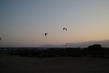 Several kitesurfers ride along the Turkish coastline at sunset. The silhouettes of kites contrast beautifully against the pastel evening sky. Ideal for themes of sport, freedom, beach holidays, and ac