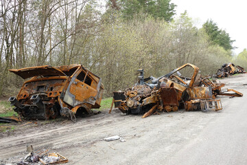 Rusty burned trucks and destroyed vehicles along an abandoned road in a forest area. Scene with wreckage and debris showing outdoor decay and industrial destruction. War in Ukraine
