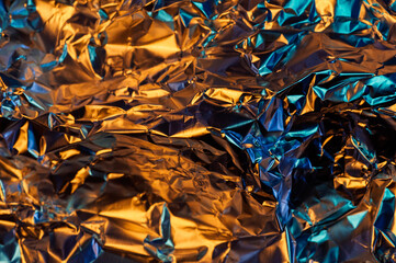 A close-up shot of crumpled aluminum foil, illuminated with a vibrant mix of orange and blue light,...