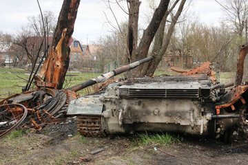 Destroyed burned tank and damaged military vehicle in a countryside village with charred trees