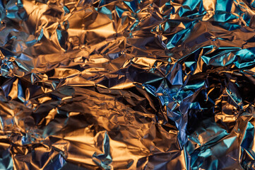 A close-up shot of crumpled aluminum foil, reflecting a mix of warm orange and cool blue light,...
