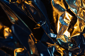 A close-up abstract shot of crumpled metallic foil, reflecting a mix of warm golden and cool blue...