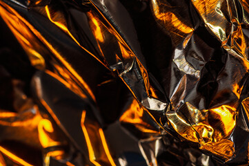 A mesmerizing close-up of crumpled metallic material, reflecting warm, golden light. The abstract...