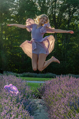 A woman in a flowing lavender dress joyfully leaps amidst a field of blooming lavender, with sunlight filtering through the trees. Her expression radiates happiness, 