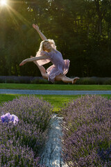 A dancer in a flowing dress leaps gracefully above a vibrant lavender field, with sunlight streaming through the trees. The scene captures a joyful moment 