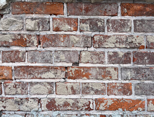 An aged and weathered brick wall exhibiting a mix of reddish-brown bricks and patches of crumbling...