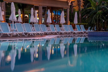 Relaxing Poolside Lounge Chairs Reflecting in Tranquil Waters During a Peaceful Evening at a Hotel...