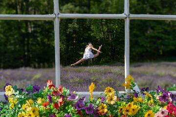 A dancer in a white dress performs a leap in a field of lavender, framed by an old-fashioned window with vibrant flowers on the sill. The lush green forest in the background
