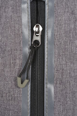 A close-up view focuses on a silver zipper with a black pull cord on a grey textile surface, showing its texture © nahhan